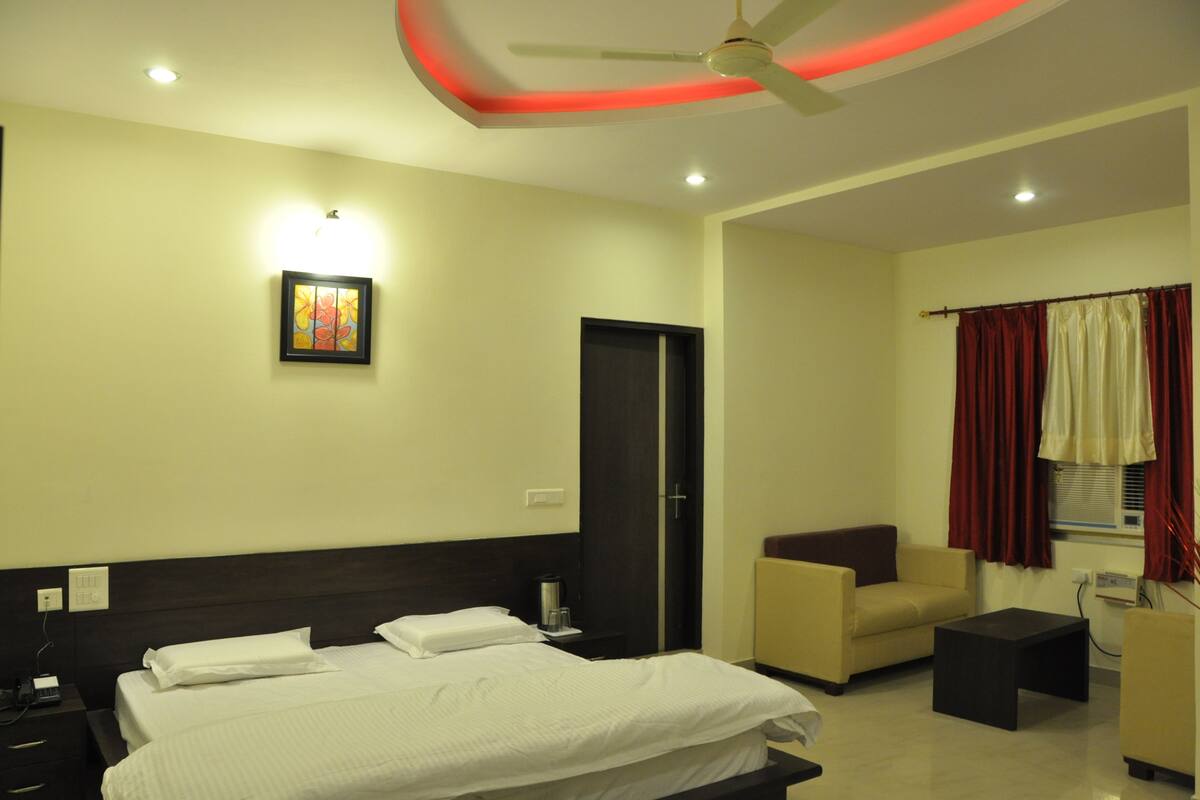 A hotel room with a bed, a chair, a small table, a ceiling fan, and a door.