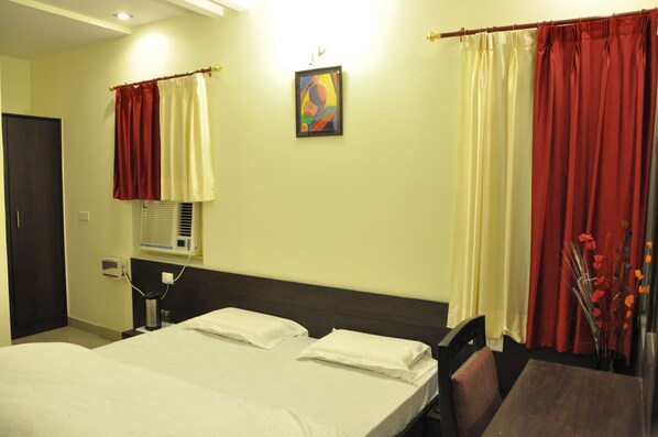 Quarto de hotel com cama, mesa de cabeceira, luminária, janela com ar condicionado e cortinas.