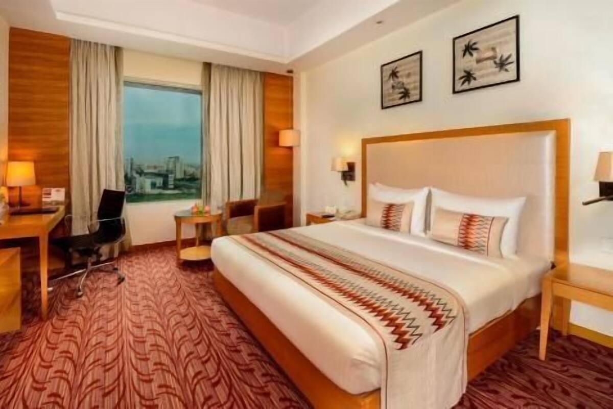 A hotel room with a large bed, a desk, a chair, a small table, and a view of the city through the window.
