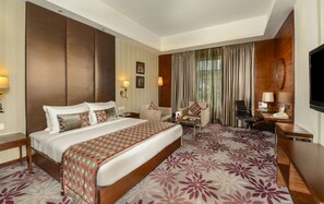 A hotel room with a large bed, a desk, a chair, and a television.