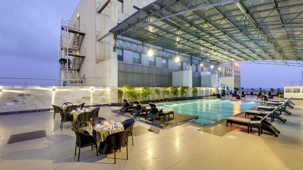 A rooftop pool area with lounge chairs and tables, a swimming pool, and a covered seating area. - Pride Plaza Hotel, Kolkata (Barasat)