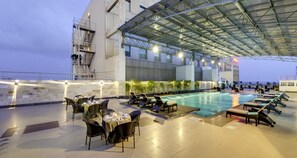 A rooftop pool area with lounge chairs and tables, a swimming pool, and a covered seating area. - Pride Plaza Hotel, Kolkata (Barasat)