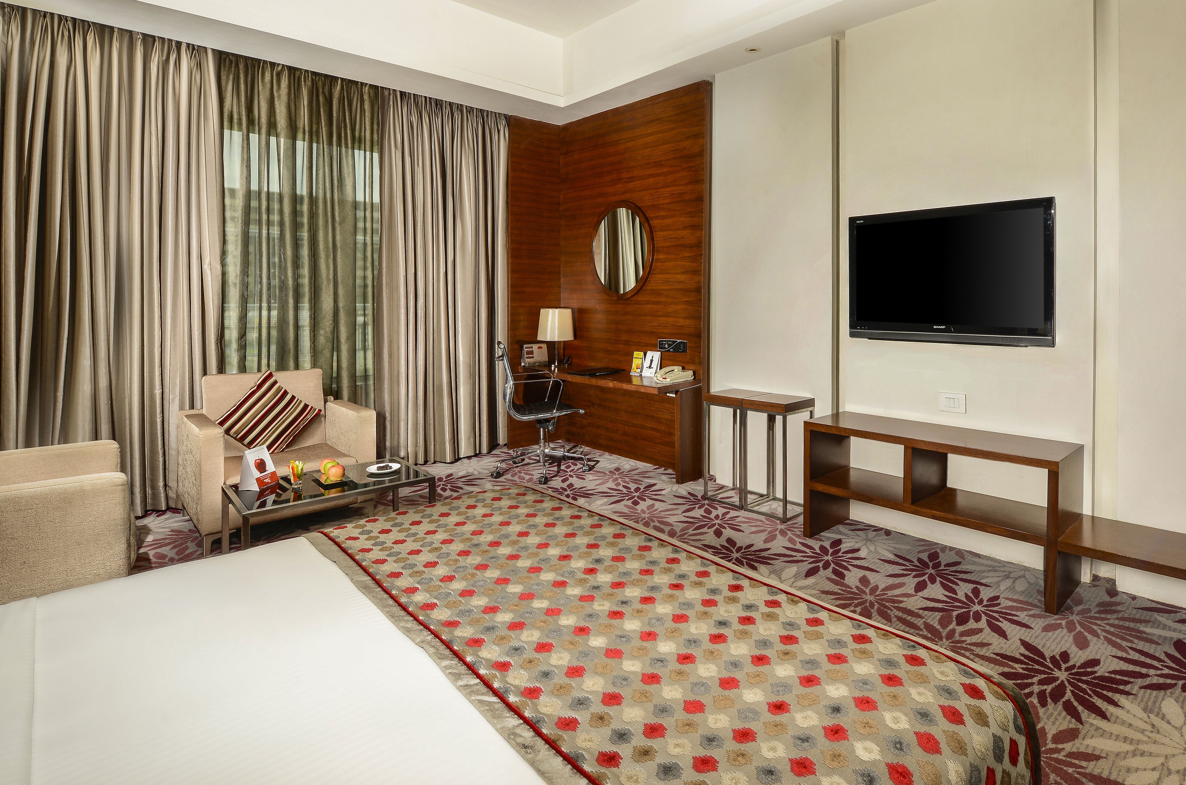 A hotel room with a large bed, a desk, a chair, a TV, and a window with curtains.