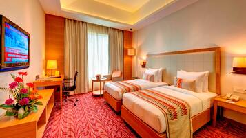 A hotel room with two beds, a desk, a chair, a TV, and a red patterned carpet.