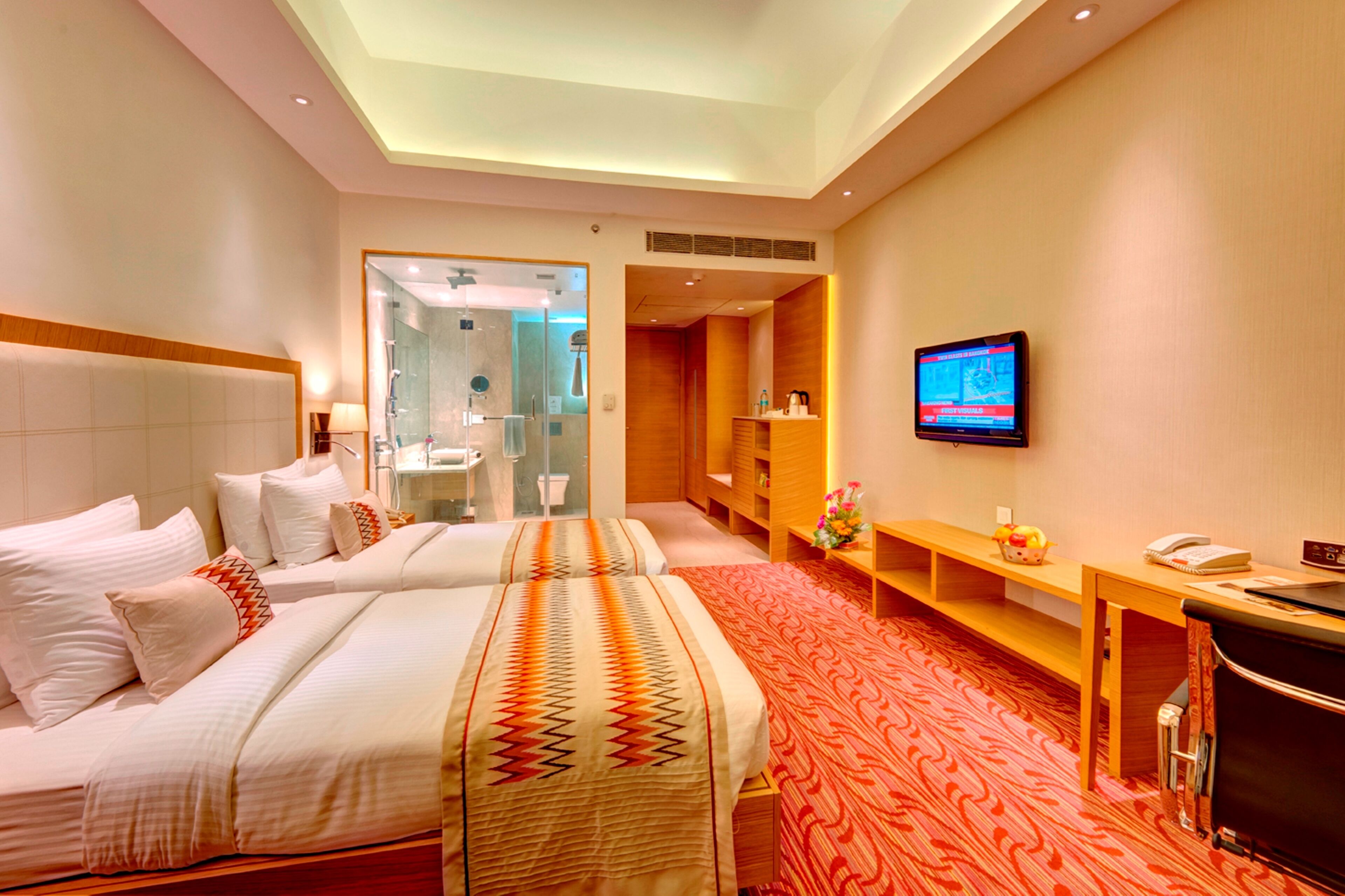 Een hotelkamer met twee bedden, een televisie, een bureau en een badkamer zichtbaar door een geopende deur.