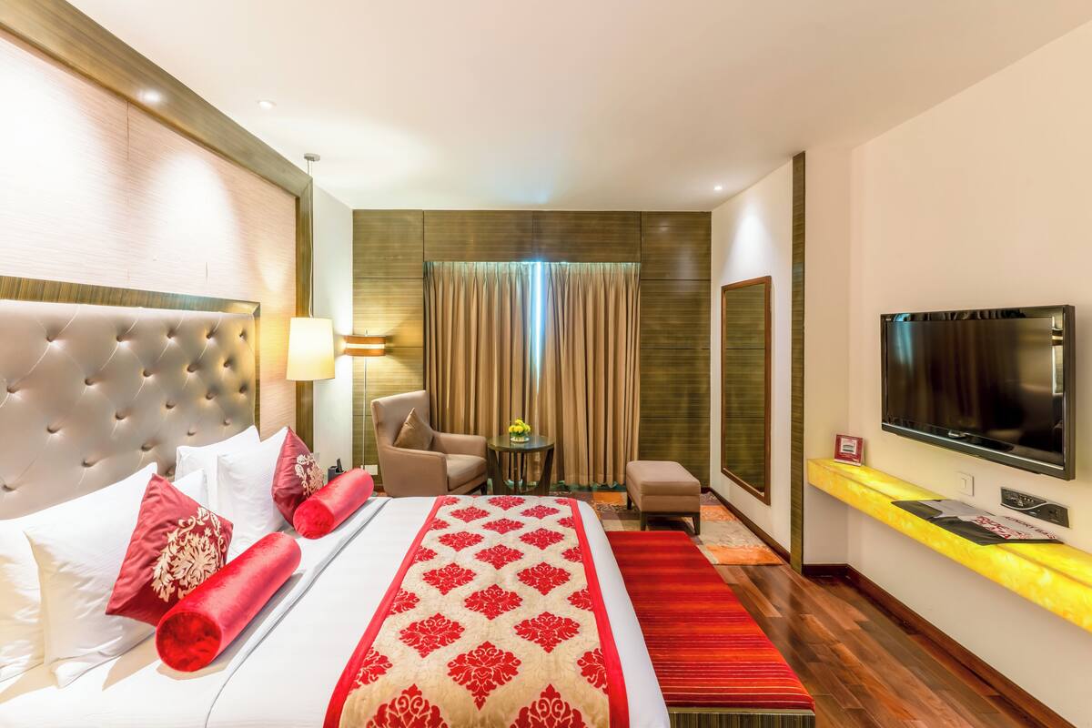 A hotel room with a large bed, a TV, a seating area, and a small table.