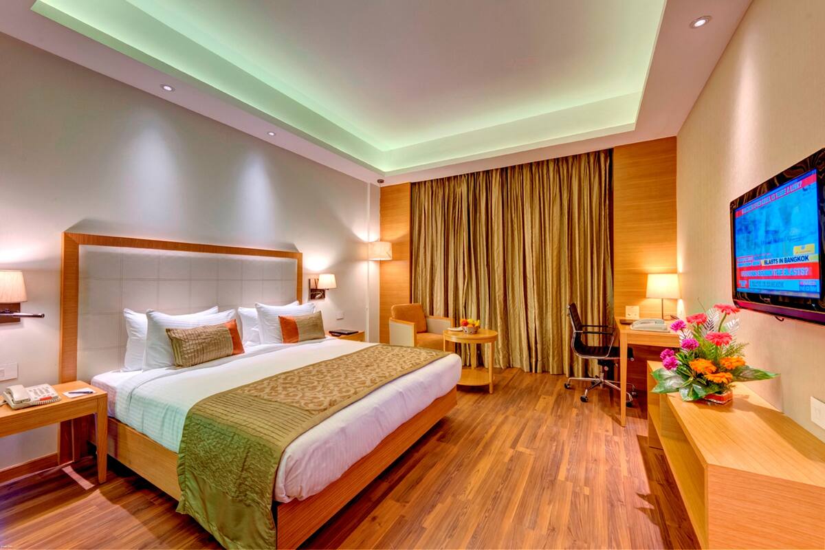 A hotel room with a large bed, a desk, a chair, a TV, and a desk lamp.