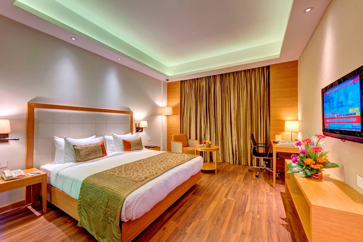 A hotel room with a bed, desk, chair, TV, and a desk lamp.