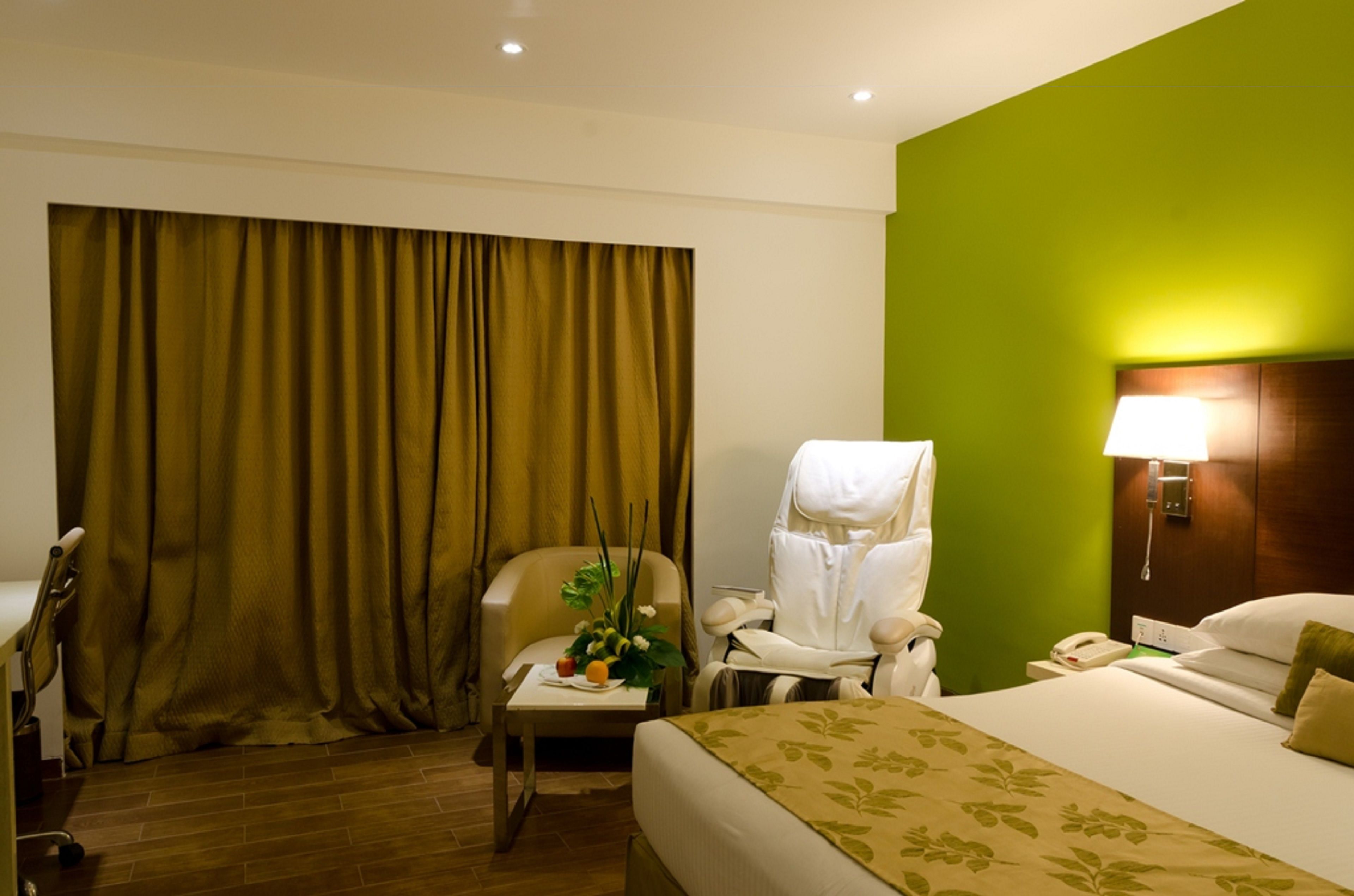 A hotel room with a bed, a chair, a desk, a lamp, and a curtain.