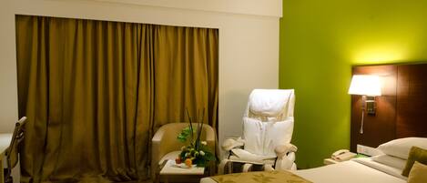 A hotel room with a bed, a chair, a desk, a lamp, and a curtain.