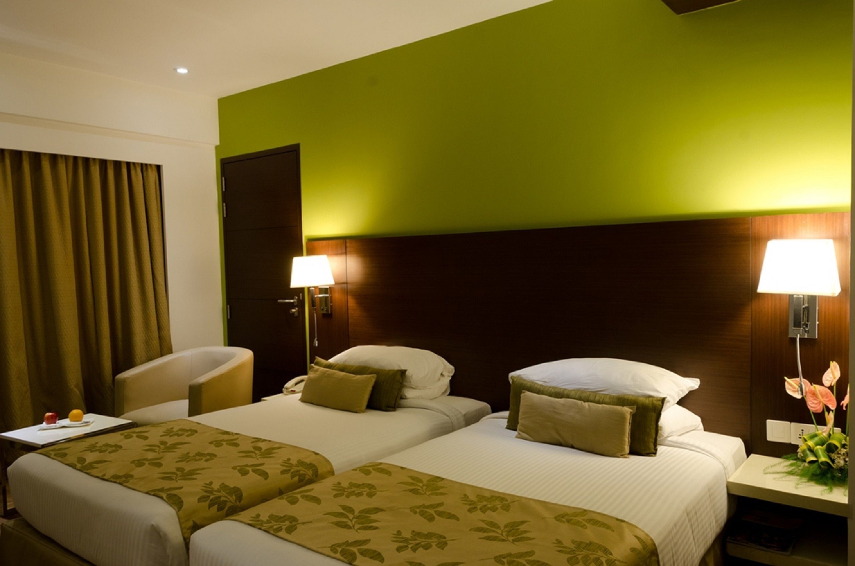 A hotel room with two beds, a desk, a chair, and a nightstand with a lamp and flowers.