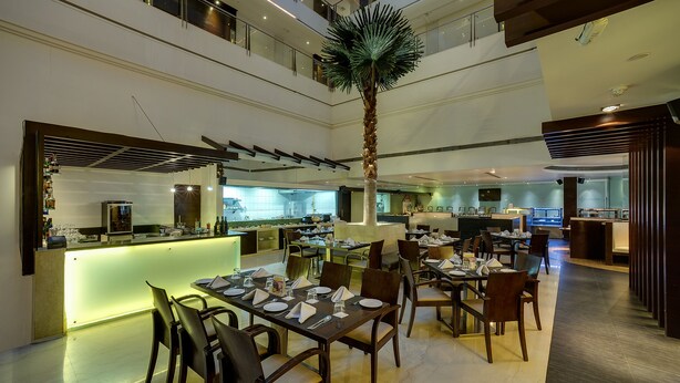 Un moderno vestíbulo de hotel con un bar central, zona de comedor y un techo alto con una palmera.