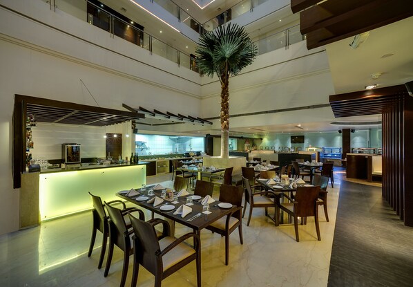 A modern hotel lobby with a central bar, dining area, and a high ceiling with a palm tree. - Ramee Grand Hotel and Spa, Pune (Pune)