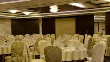 Un salón de banquetes con mesas redondas cubiertas con manteles blancos, sillas con fundas blancas y piso alfombrado.