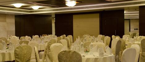 Un salón de banquetes con mesas redondas cubiertas con manteles blancos, sillas con fundas blancas y piso alfombrado.