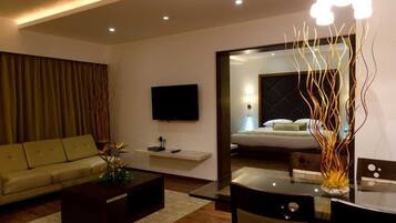 A modern hotel room with a sofa, a coffee table, a TV, a bed, and a decorative vase.