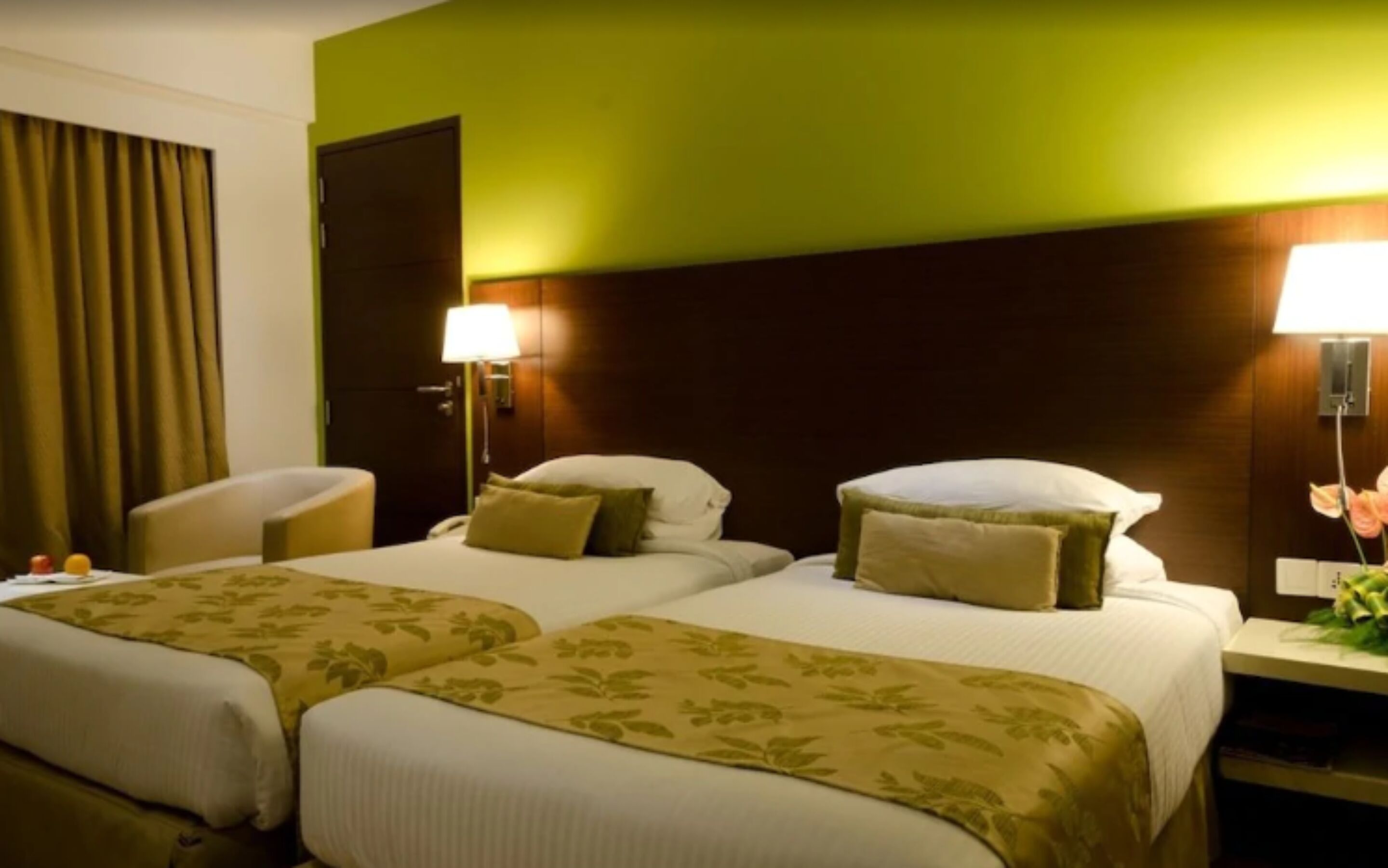 A hotel room with two beds, a chair, a desk, and a lamp.
