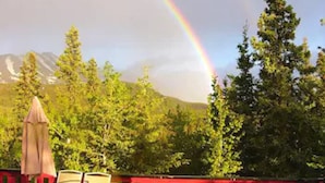 An outdoor seating area with a table and chairs, a red railing, and a mountain backdrop.