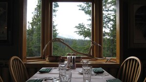 A dining table set for two with a view of a forest through large windows.