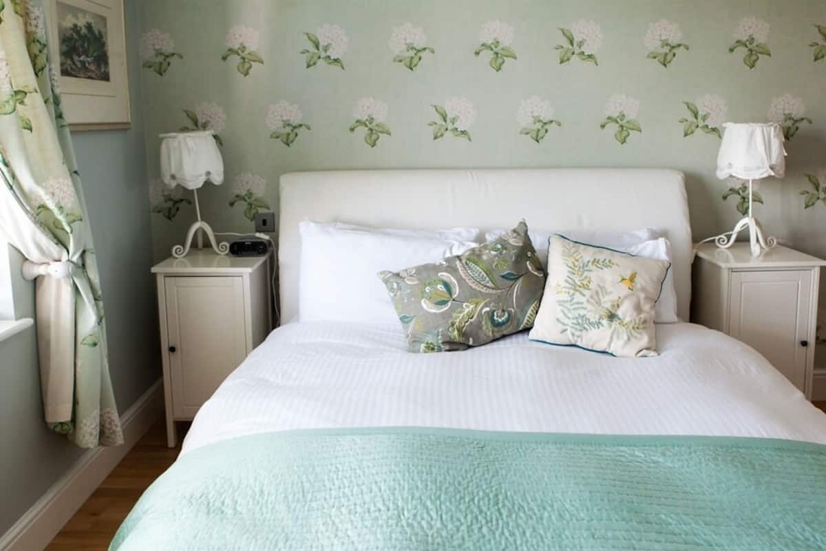 A neatly made bed with a white headboard, two bedside tables with lamps, and floral wallpaper.