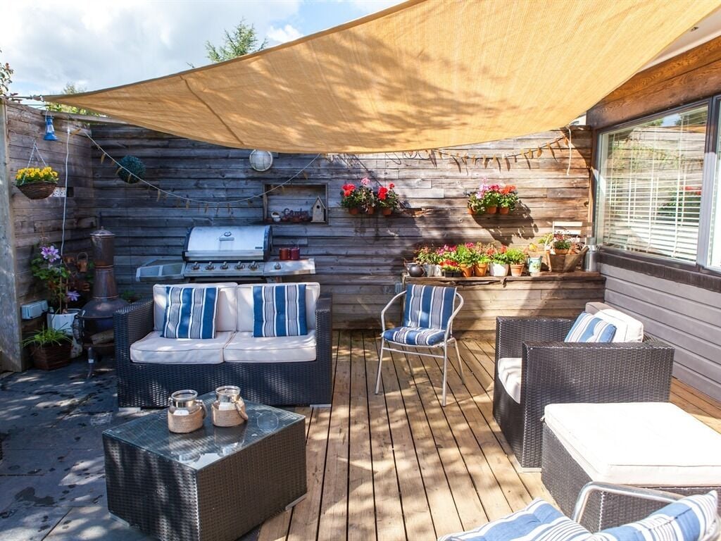 Un patio al aire libre con terraza de madera, mobiliario de mimbre, una parrilla y plantas en macetas.