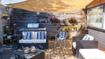 Un patio al aire libre con terraza de madera, mobiliario de mimbre, una parrilla y plantas en macetas.