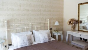 A neatly arranged bedroom with a bed, a bedside table, a lamp, a mirror, and a small bench. - Birch House B&B (Weymouth)