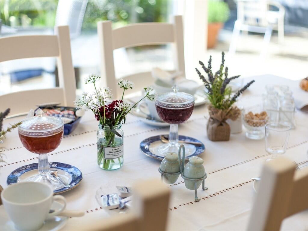 Une table dressée avec un verre de vin rouge, un verre de vin blanc, un petit vase avec des fleurs, des salières et des poivrières, et une plante décorative.