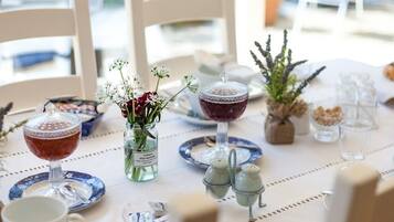 Une table dressée avec un verre de vin rouge, un verre de vin blanc, un petit vase avec des fleurs, des salières et des poivrières, et une plante décorative.