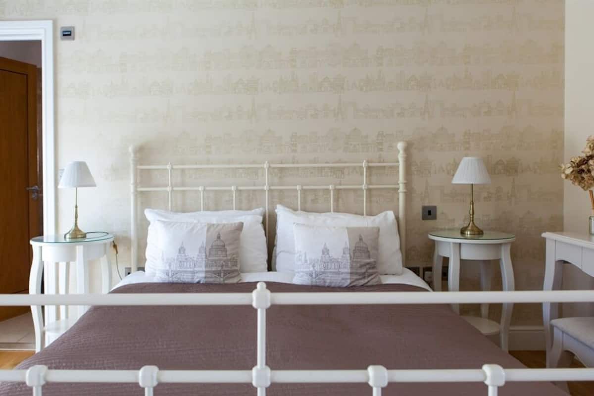 A double bed with a white metal frame, two bedside tables with lamps, and a wall with a cityscape wallpaper.