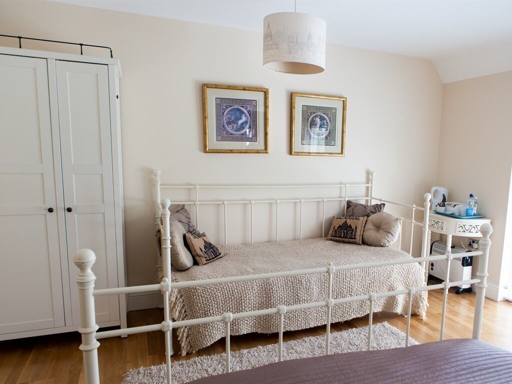 A bedroom with a white metal bed frame, a white wardrobe, and a small bedside table with a lamp.