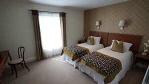 A hotel room with two beds, a desk, a chair, and a window with curtains.