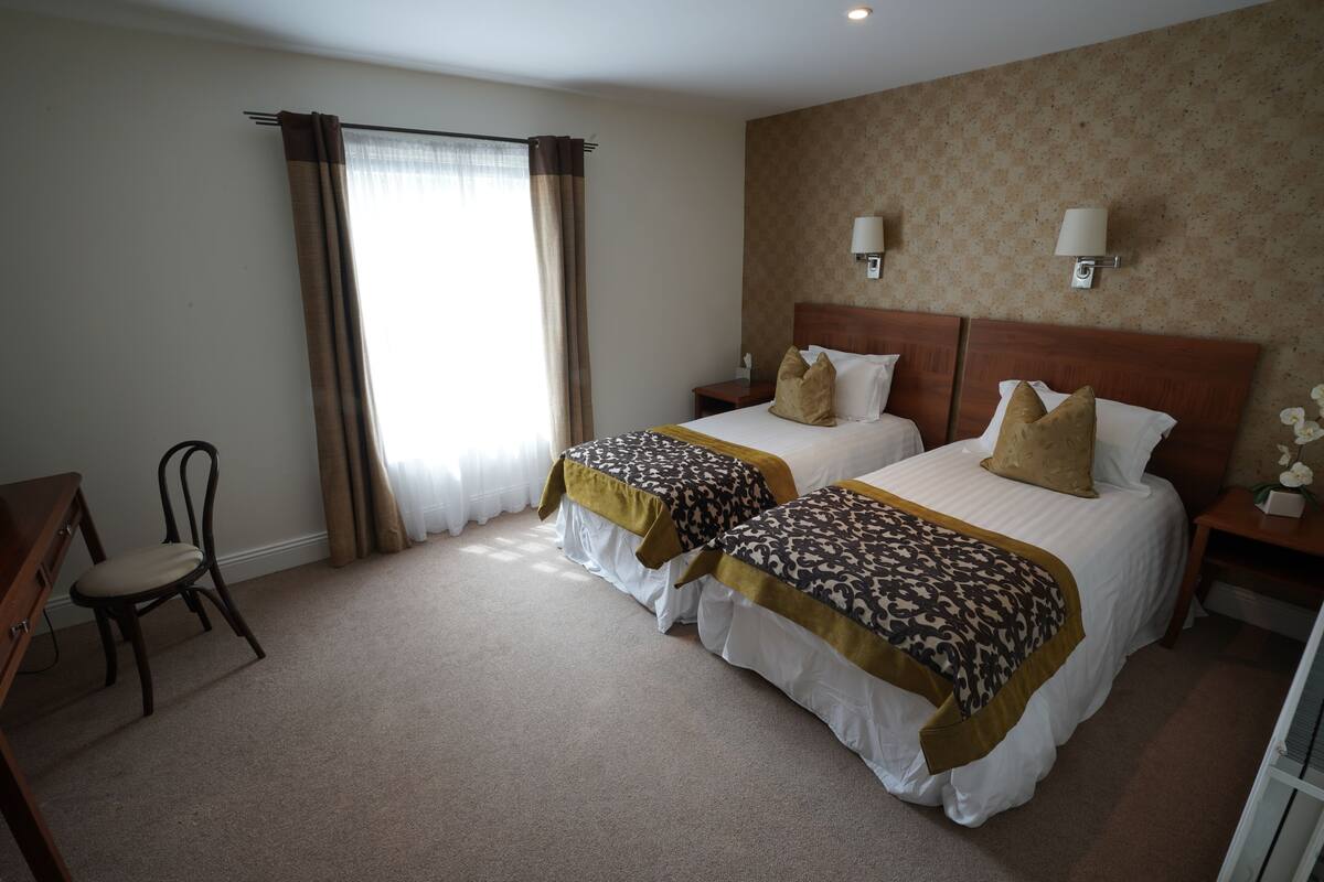 A hotel room with two beds, a desk, a chair, and a window with curtains.