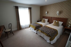 Quarto de hotel com duas camas, uma mesa, uma cadeira e uma janela com cortinas.