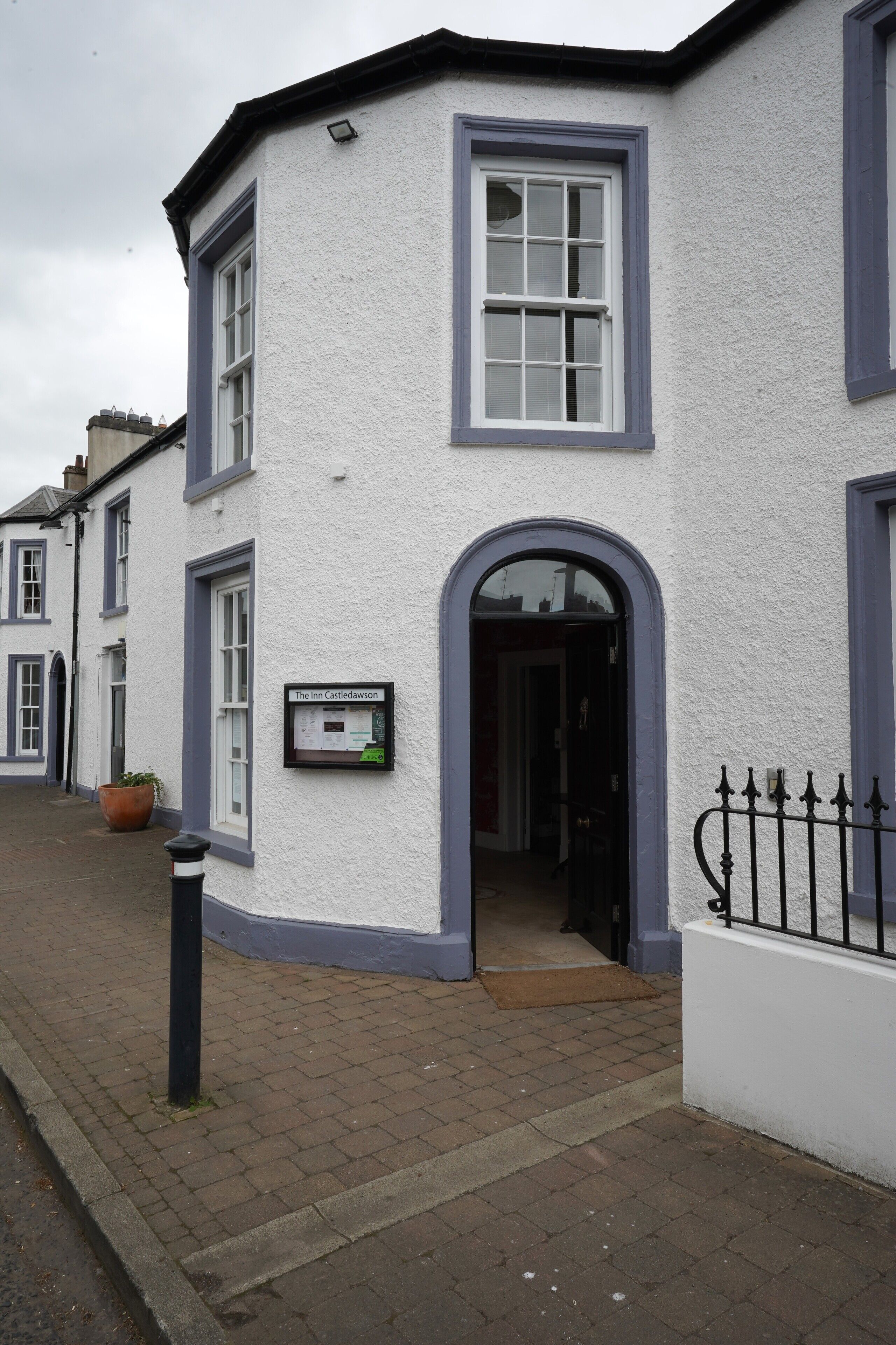 A white building with a blue door and windows, a sign reading "The Inn Castlewood," and a black metal fence.