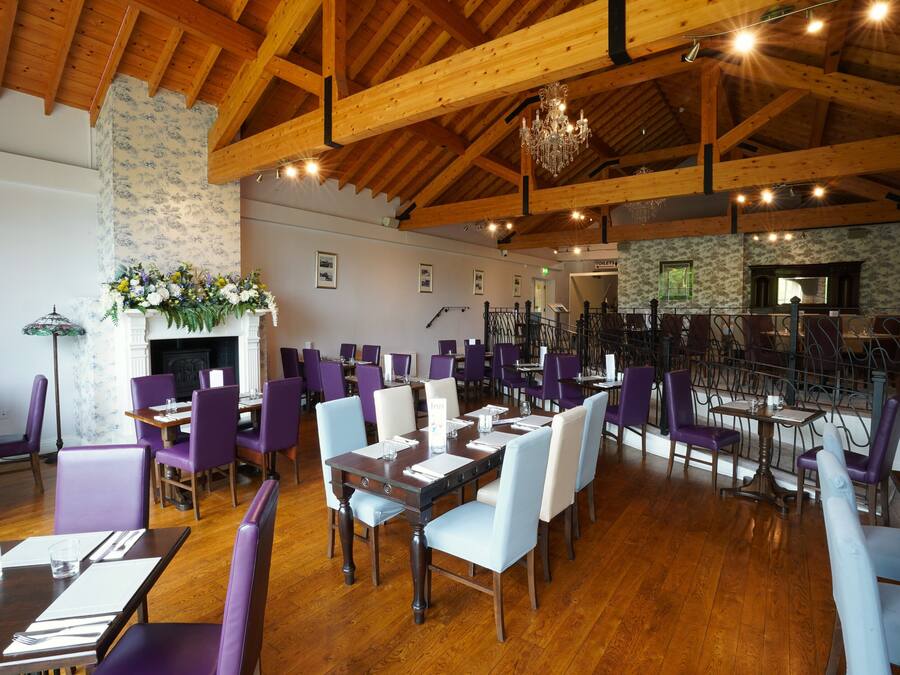 A restaurant with wooden beams, purple and white chairs, and a chandelier.
