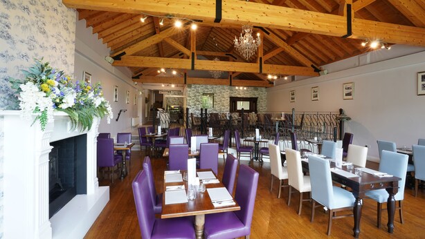 A restaurant with wooden beams, purple and white chairs, and a fireplace.