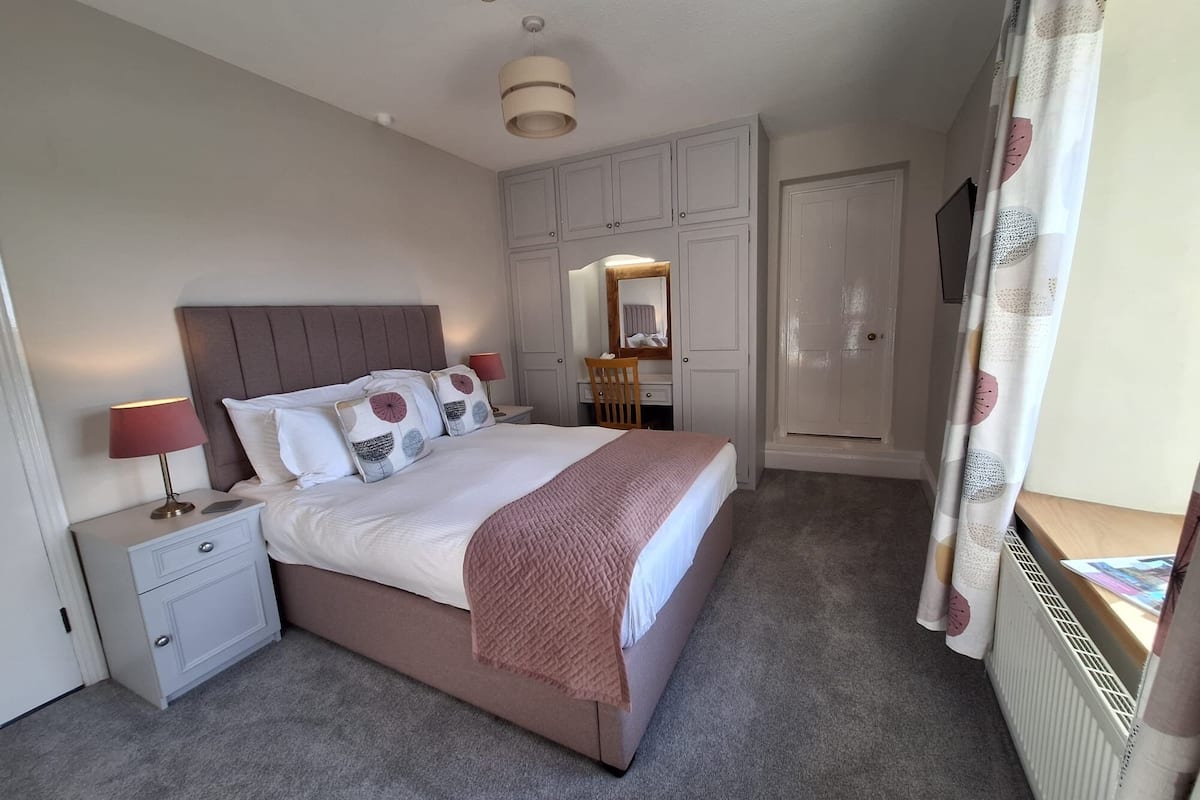 A bedroom with a bed, nightstands, a mirror, a wardrobe, and a radiator.