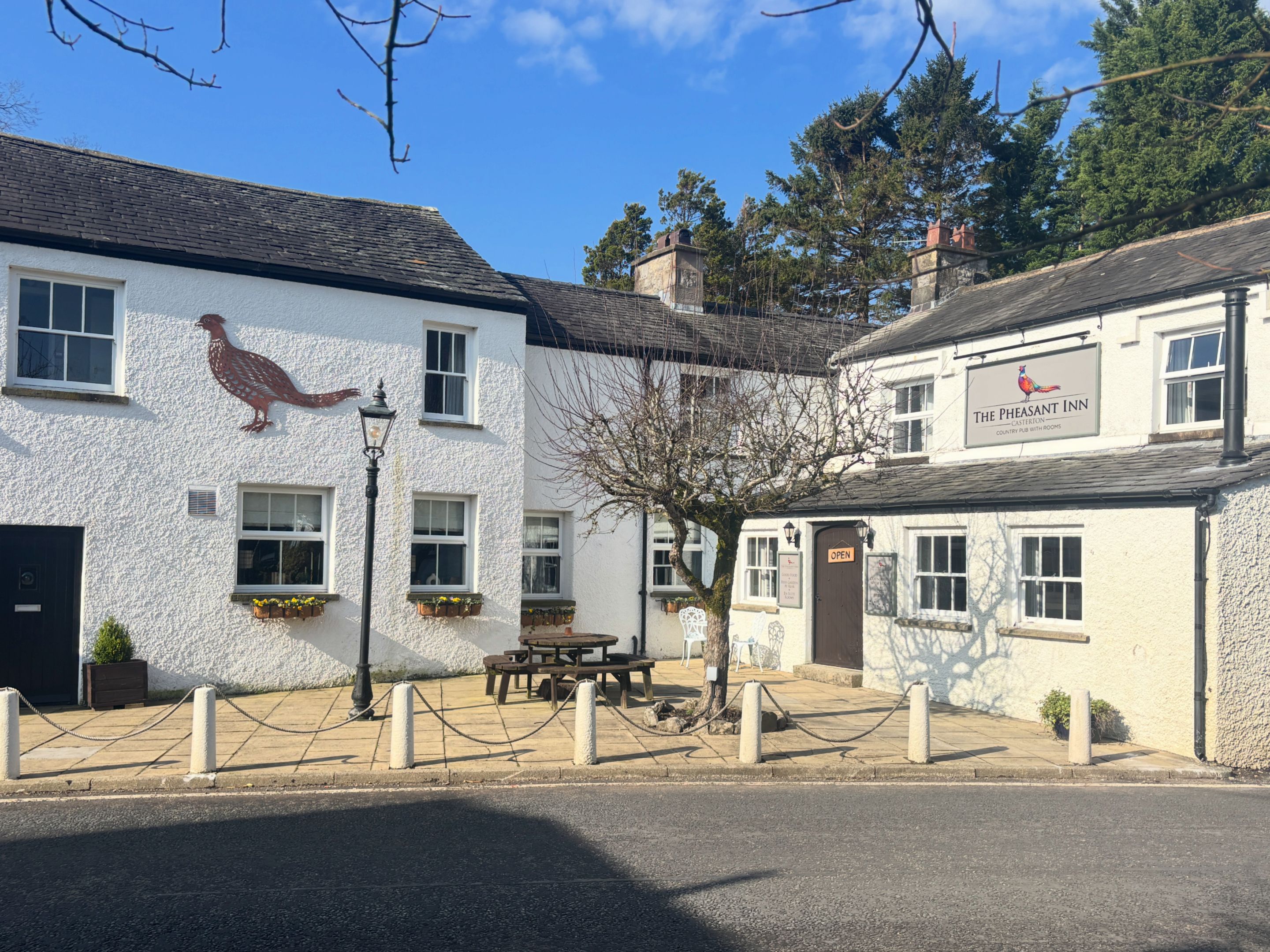 Un edificio con fachada blanca, un letrero que dice 'The Pheasant Inn' y mesas al aire libre.