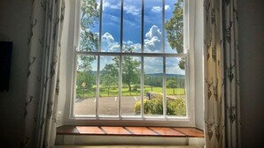 Une fenêtre donnant sur un paysage verdoyant, un ciel dégagé et un banc en bois à l’intérieur.