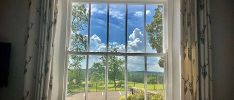 A window with a view of a green landscape, a clear sky, and a wooden bench inside.