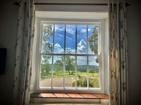 Una ventana con vistas a un paisaje verde, cielo despejado y un banco de madera en el interior.