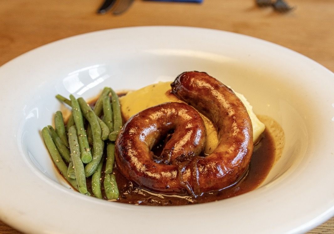 A plate with a sausage, green beans, and mashed potatoes.