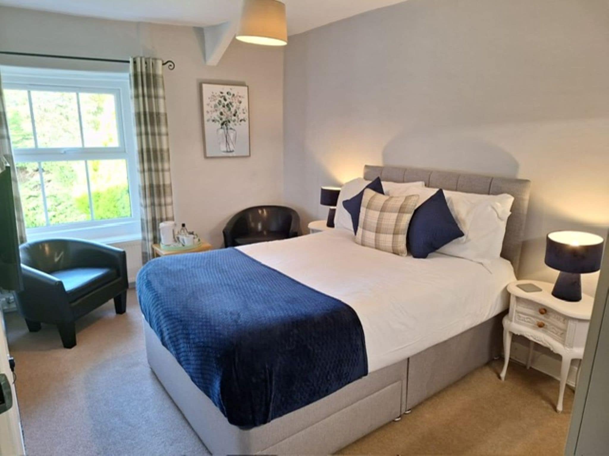 A bedroom with a large bed, bedside tables, a chair, a window, and a painting on the wall.