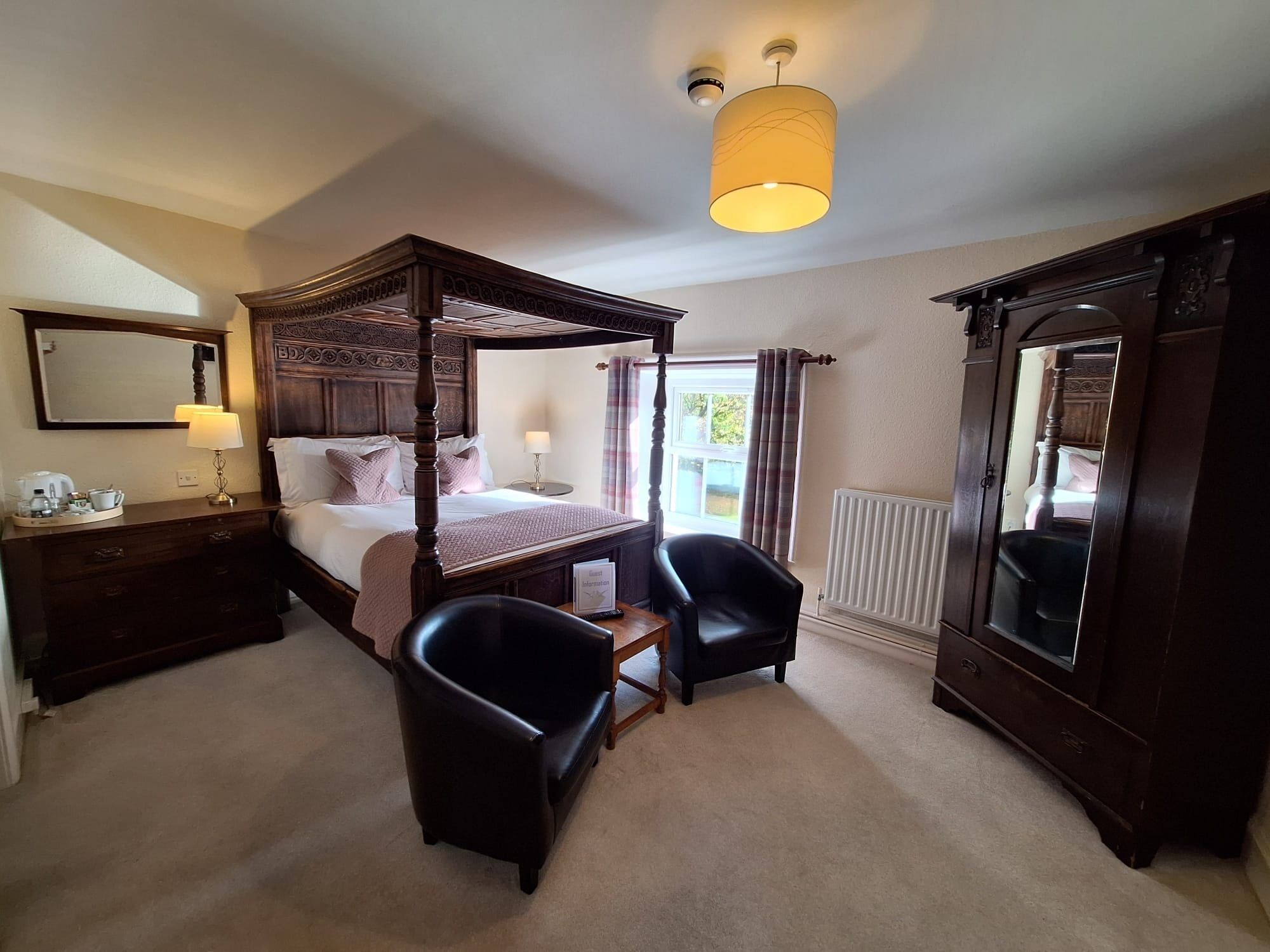 A four-poster bed with a canopy, a bedside table with a lamp, a chair, a large mirror, and a radiator.