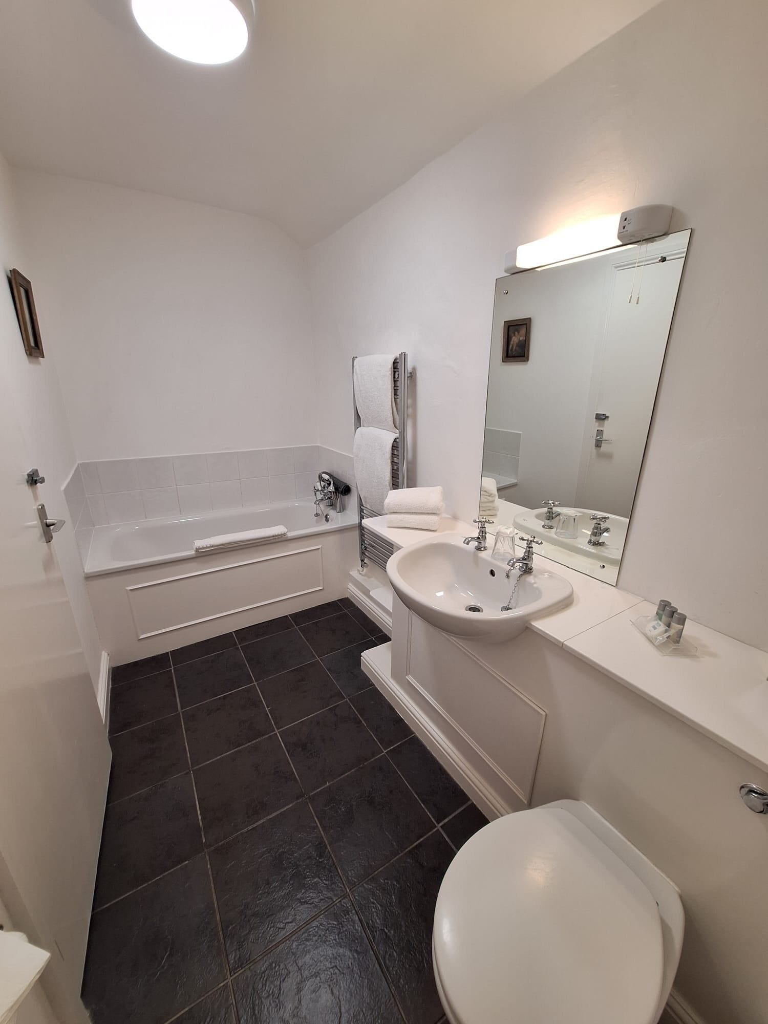 Un baño moderno con bañera, lavamanos, inodoro y un espejo grande.