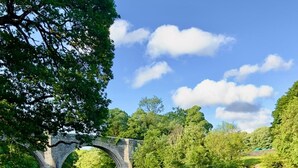 Un pont de pierre enjambe une rivière paisible, bordée de part et d’autre d’une végétation luxuriante.