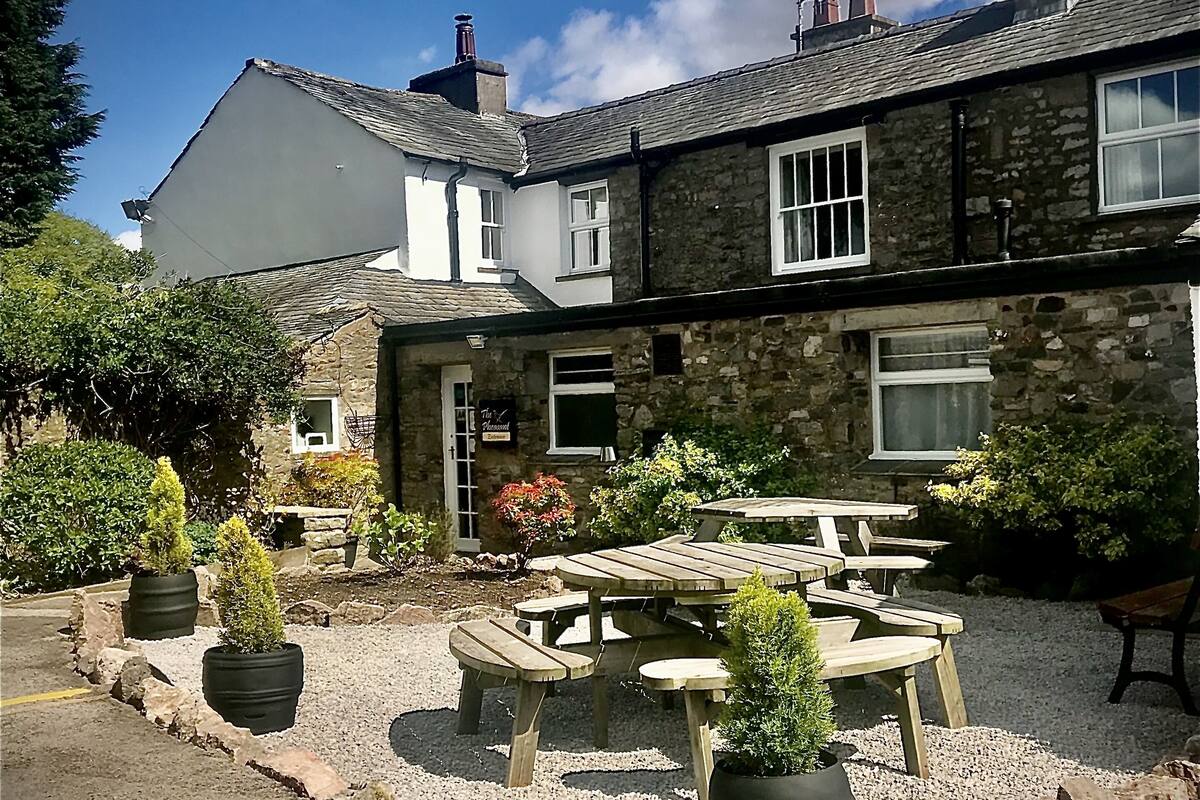 A stone building with a patio area featuring wooden tables and benches, surrounded by potted plants.