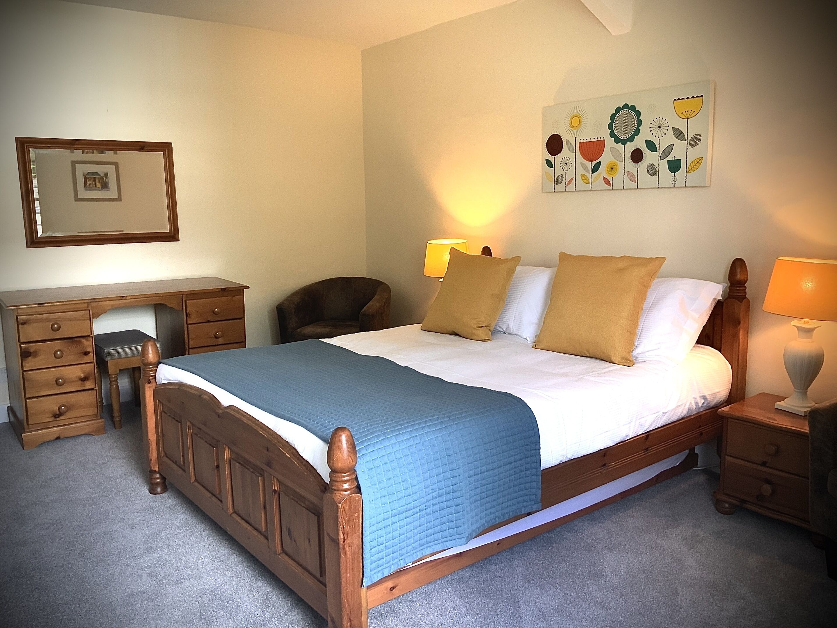 A bedroom with a wooden bed, a desk, a chair, and a wall-mounted lamp.