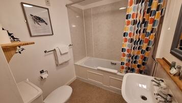 Ein Badezimmer mit Toilette, Waschbecken, Badewanne, Duschvorhang und einem gerahmten Bild an der Wand.